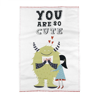 Tea towel reading You are so cute, and little red heart shapes above a green horned monster holding a Love card, hugged by a girl in a blue dress. Off-white ground.