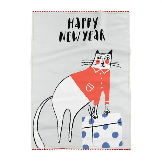 Tea towel printed on a pale grey ground, reading Happy New Year, above a white cat in a red top standing beside a blue spotted gift box